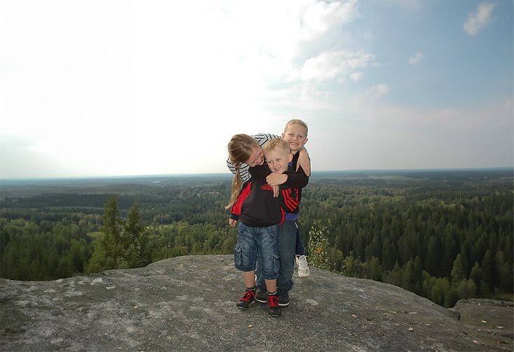 tre barn står på ett berg med utsikt i bakgrunden.