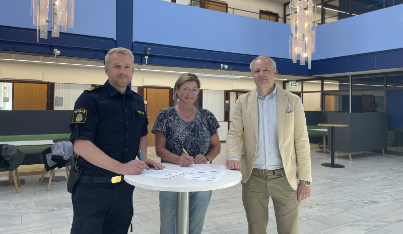 Lokalpolisområdeschef Anders Sund tillsammans med kommunalråden Marie och Anton står vid ett bord i kommunhusets ljushall.