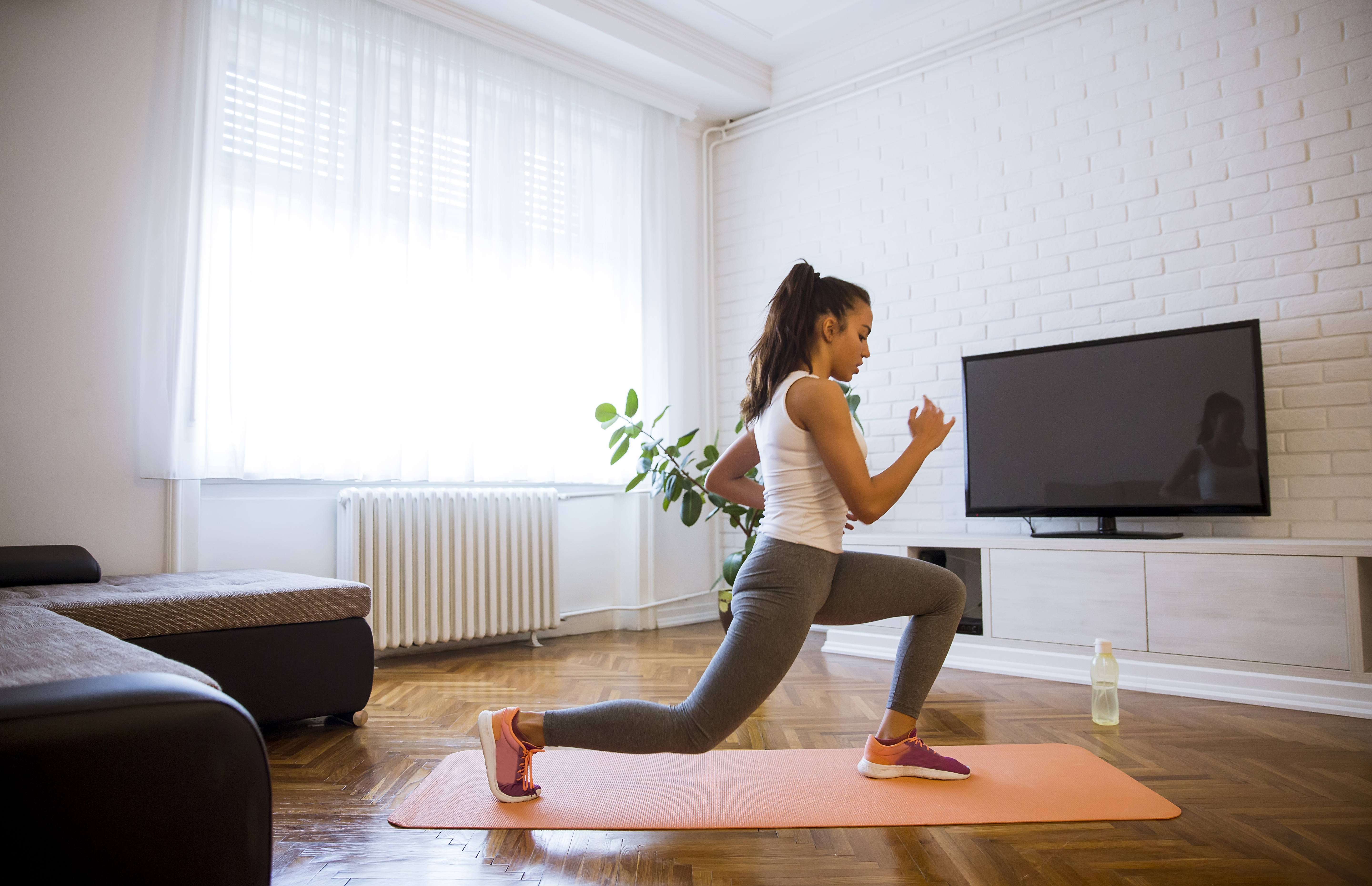 En ung tjej som tränar på en yogamatta i ett vardagsrum. 