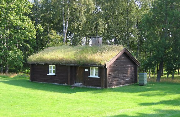 en liten brun stuga med gräs på taket