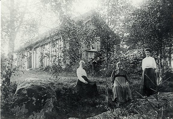 en svartvit bild på tre kvinnor i olika åldrar framför ett hus.