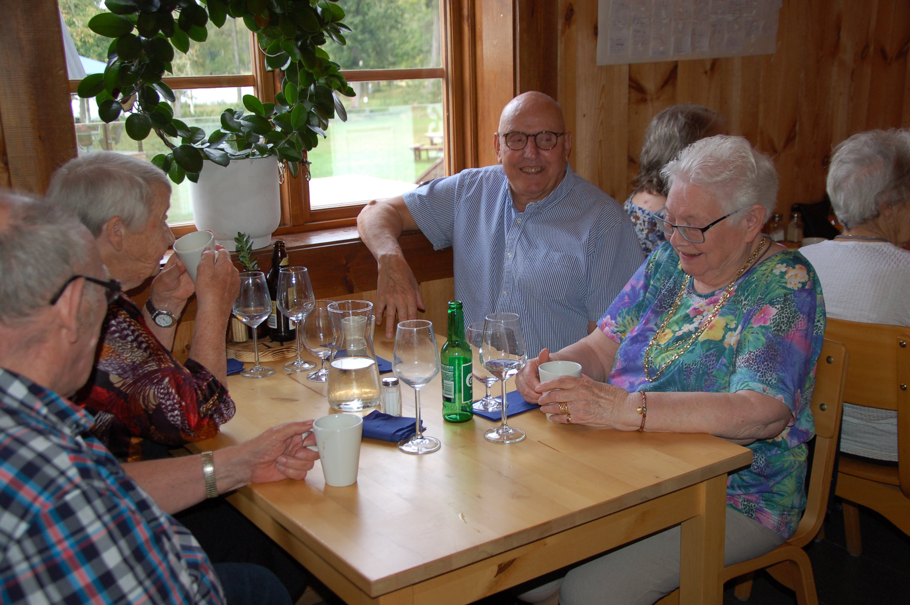 Fyra glada pensionärer sitter vid ett bord på restaurang samtalar och väntar på sin mat.