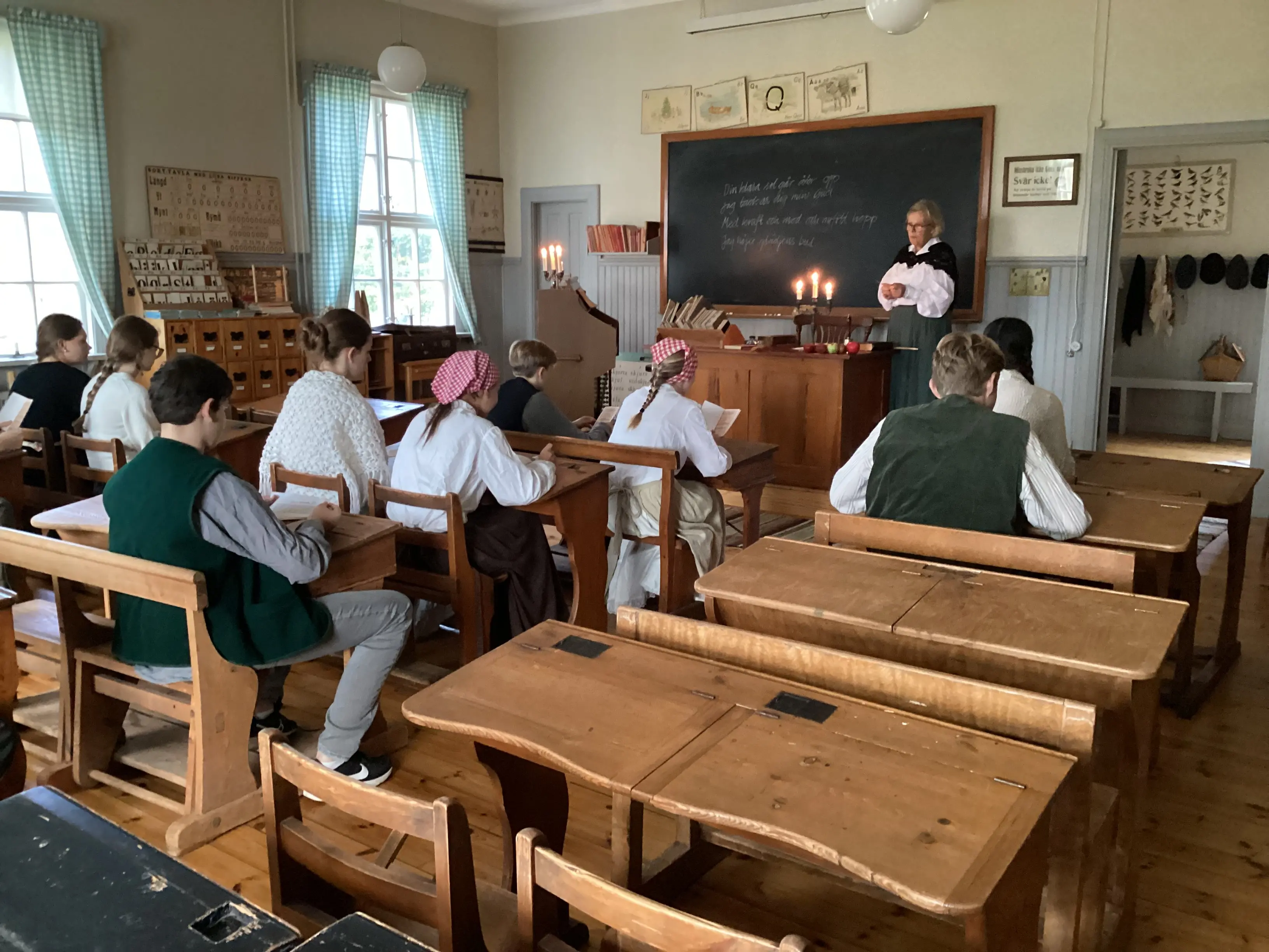 Ett foto som visar en gammaldags skolsal med elever och en fröken vid katedern.