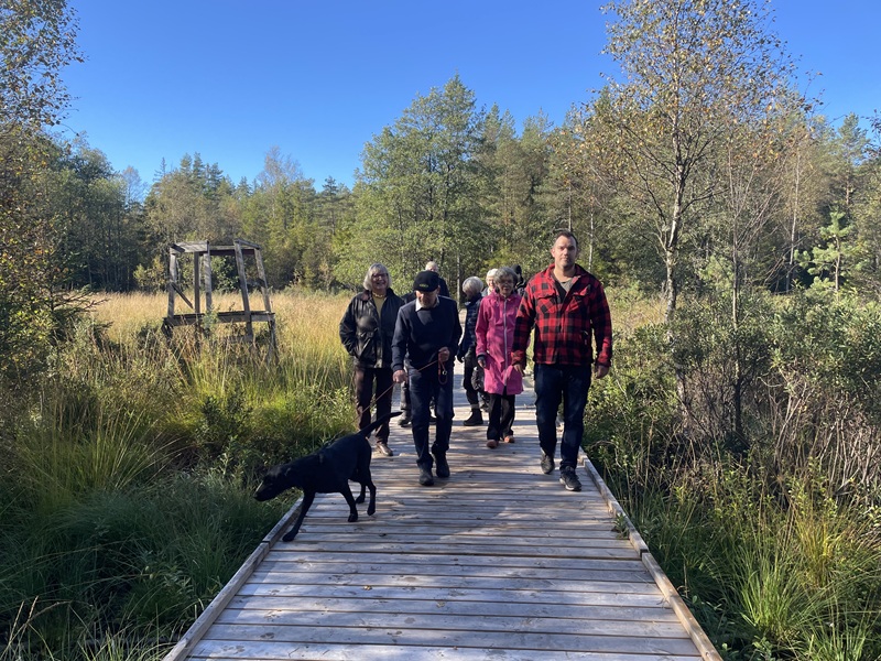 En spång i trä där ett 10-tal personer och en hund vandrar framåt.