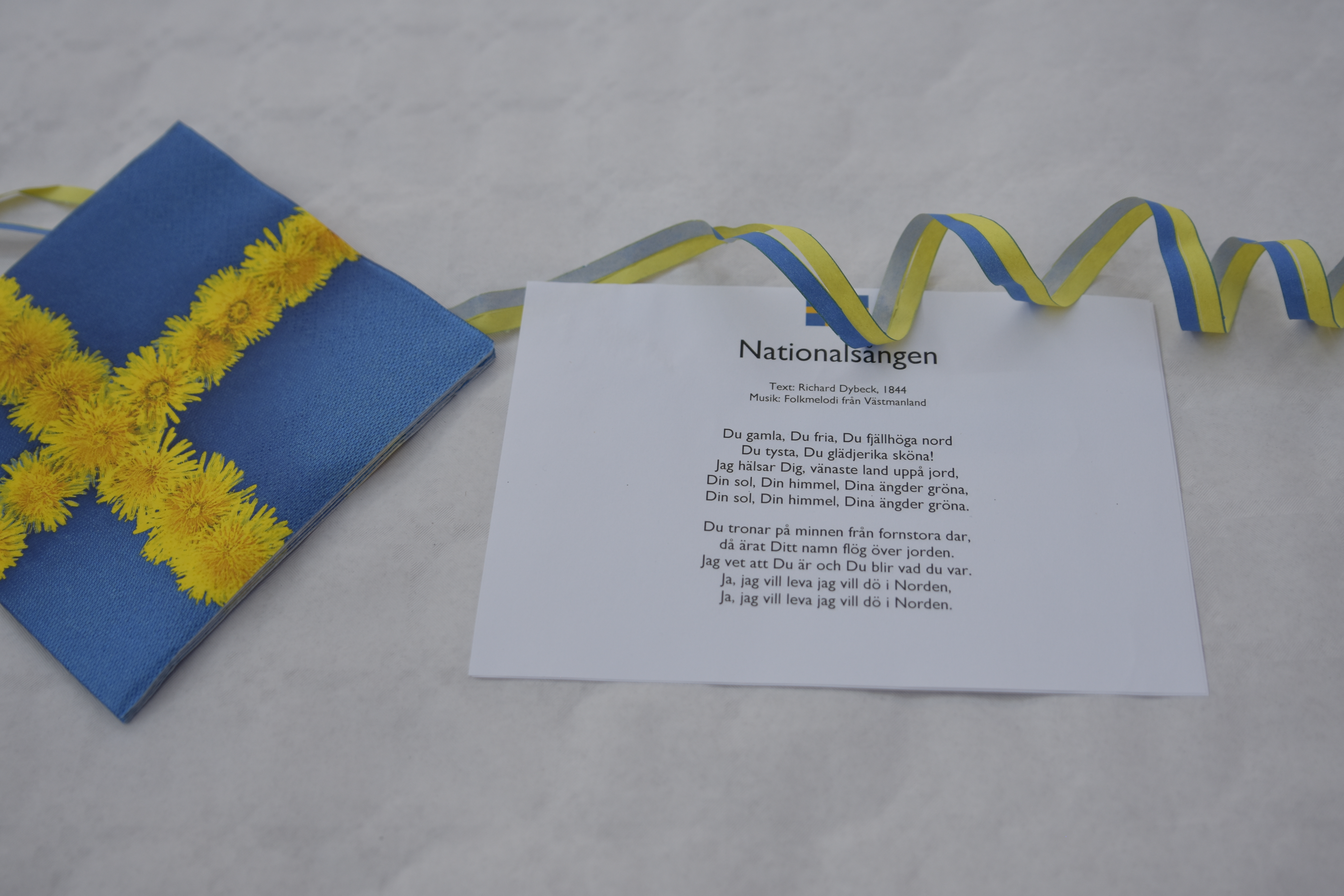 Ett papper med texten till "Du gamla du fria" och en servett med svenska flaggan på.