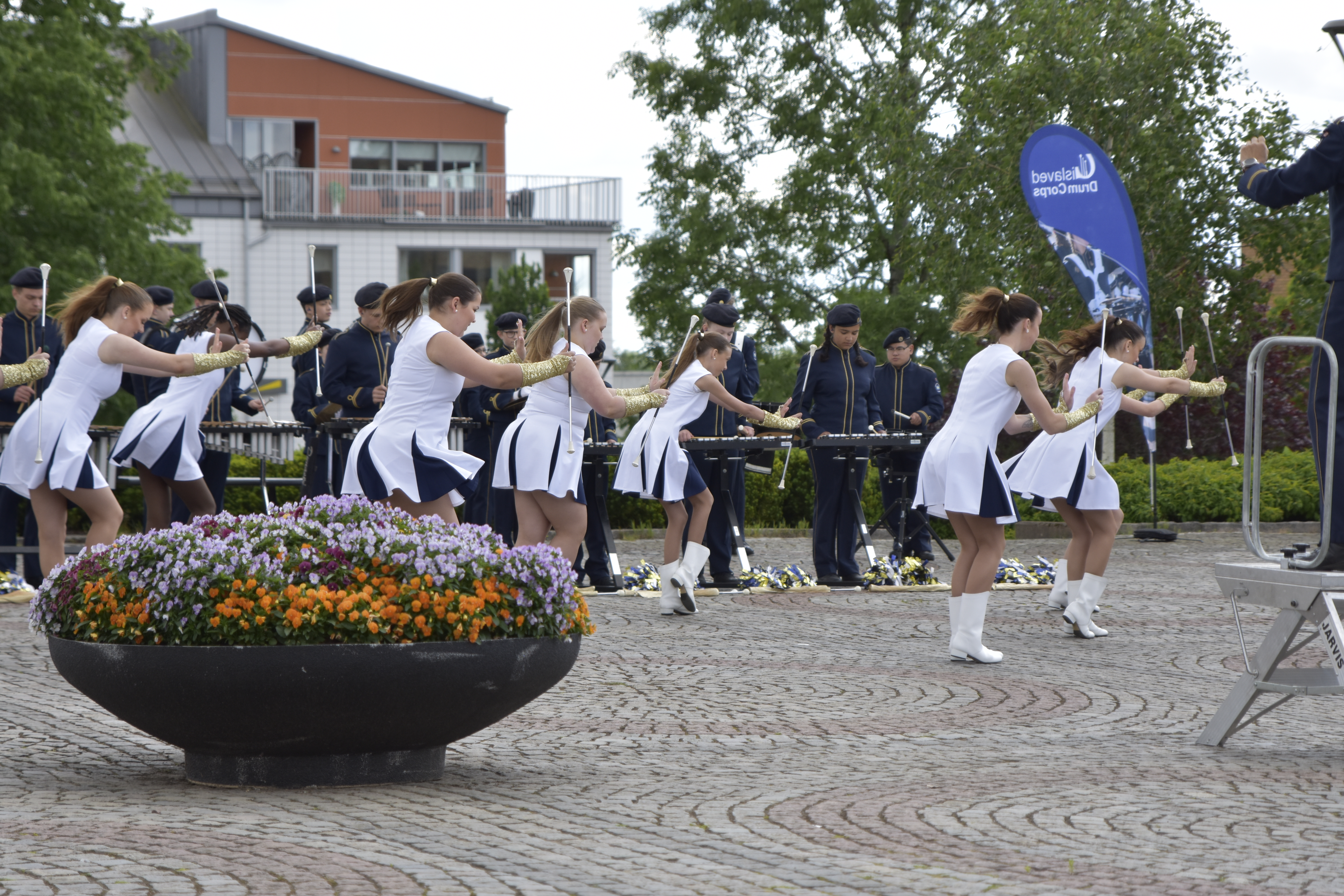 Drillande flickor i vita klänningar på ett torg.