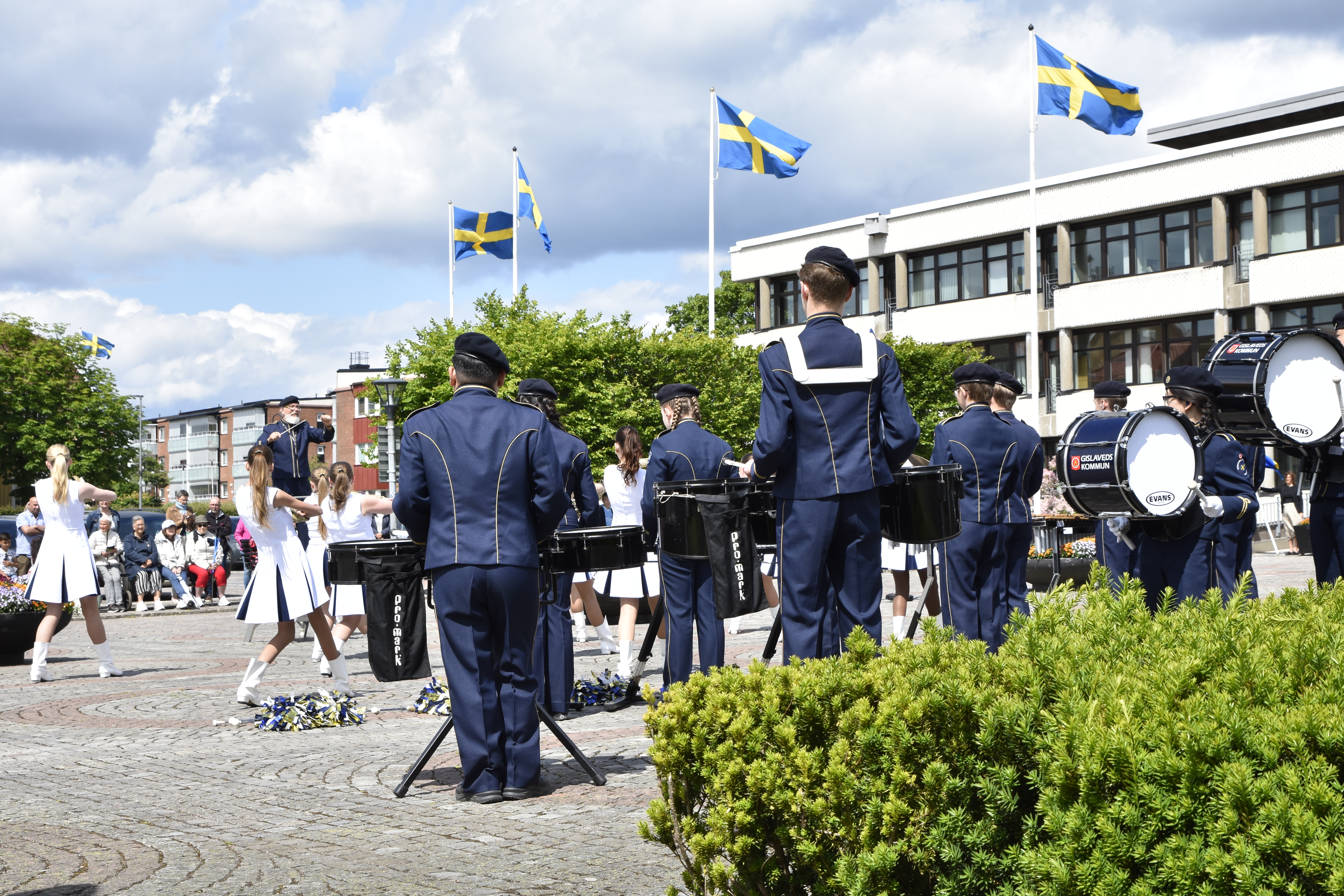 Ett tiotal personer som spelar instrument. I bakgrunden syns kommunhuset och flaggstänger med svenska flaggan hissad.