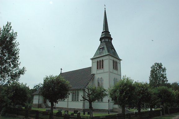 en gammal vit kyrka med ett spetsigt torn och  höga fönster.