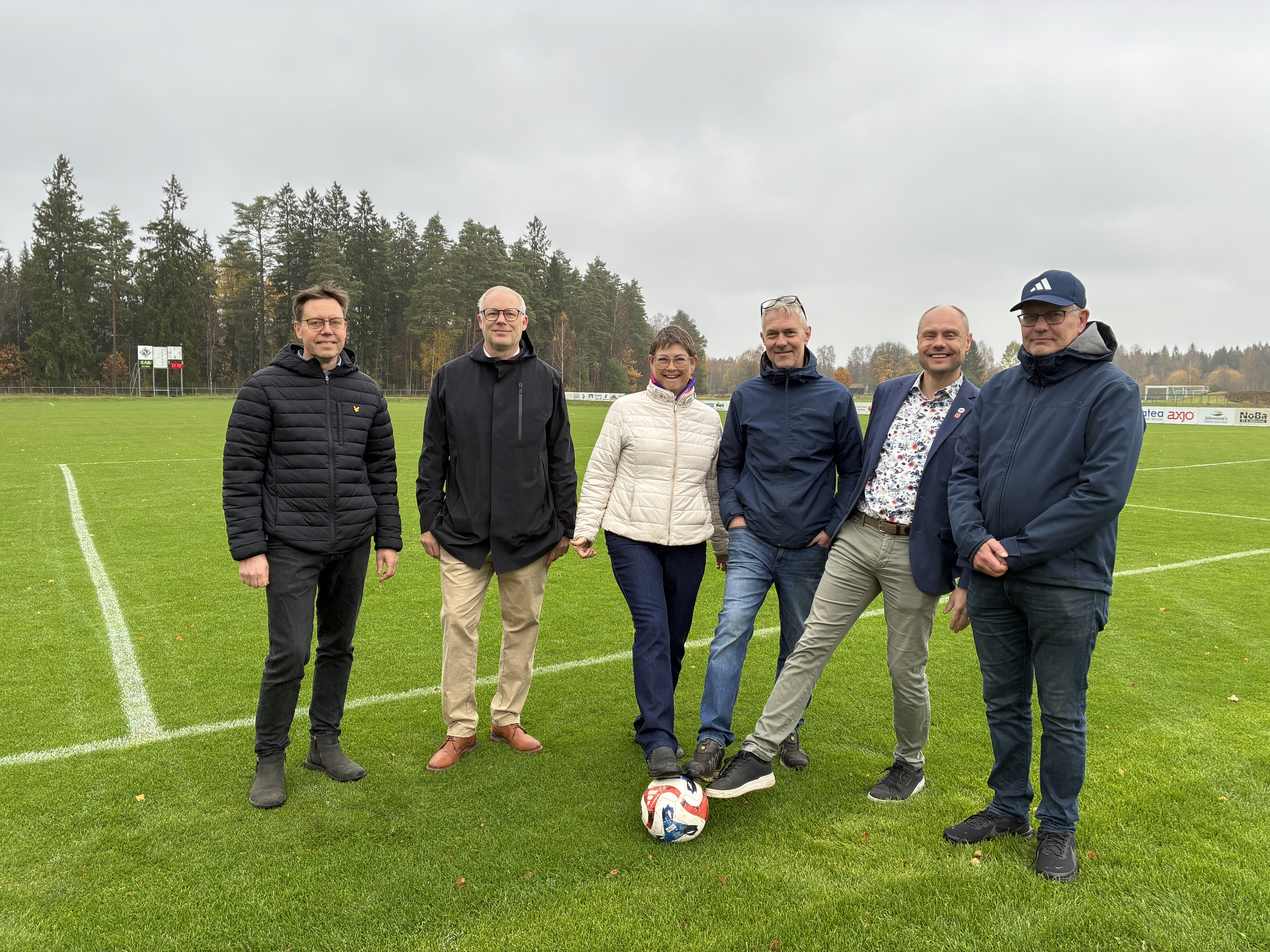 En grupp människor står med en fotboll framför en fotbollsplan