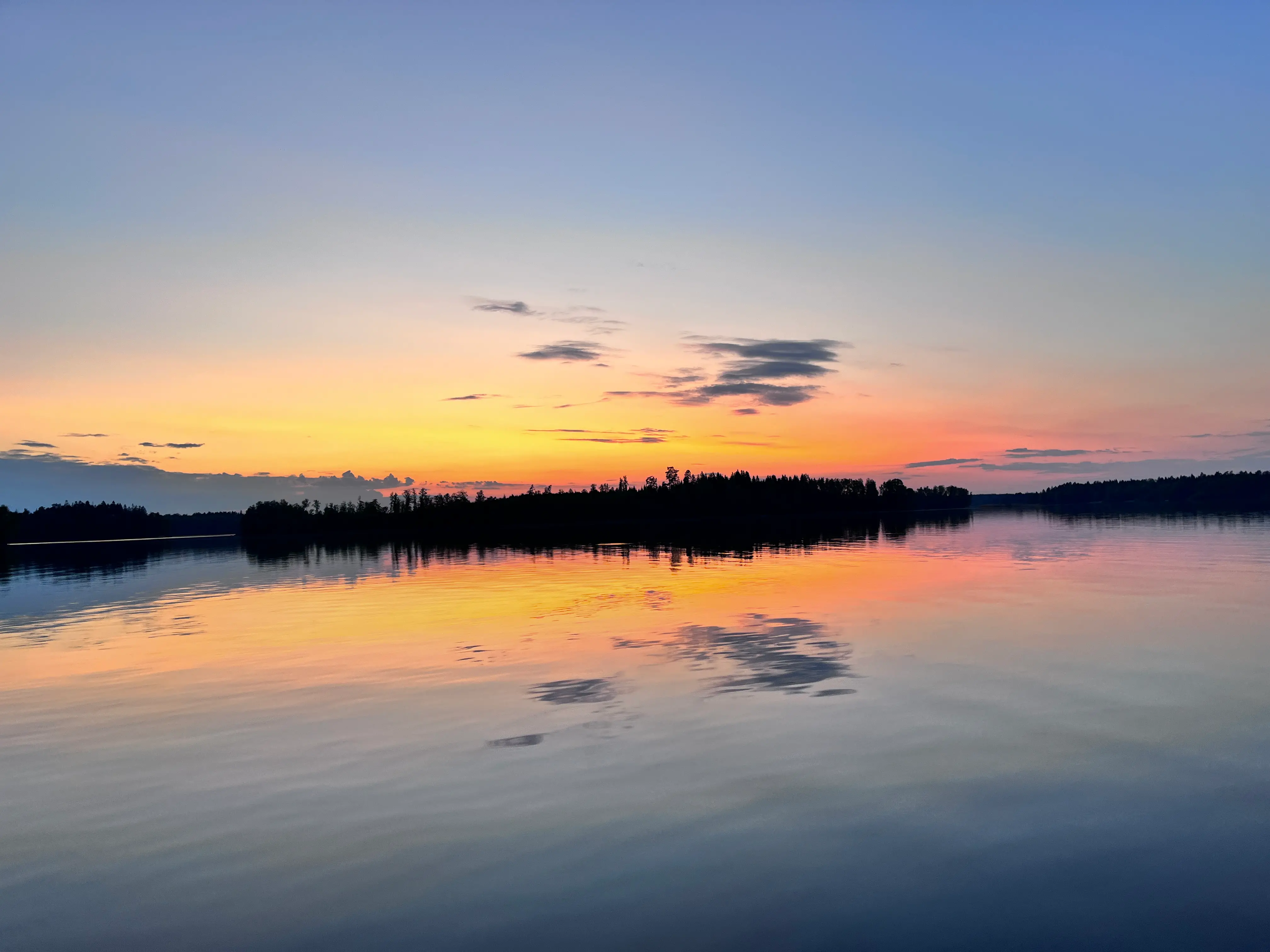 Solnedgång över sjön Bolmen. Foto taget från en båt och man ser solen spegla sig i det stilla vattnet.