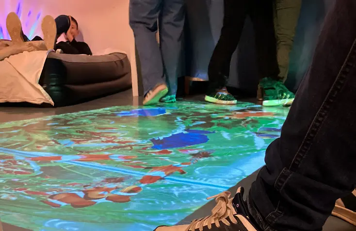 Bild på ett golv som ett digital spel projiceras på. Man ser fötter som ska hoppa på figurer som rör på sig.