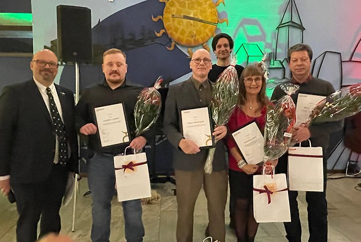 6 personer står bredvid varandra med diplom och papperskassar i händerna.