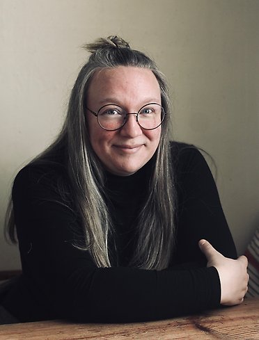 en småleende kvinna i glasögon och delvis uppsatt hår tittar in i kameran.