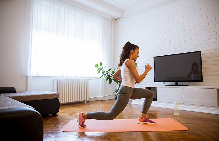 En ung tjej som tränar på en yogamatta i ett vardagsrum. 