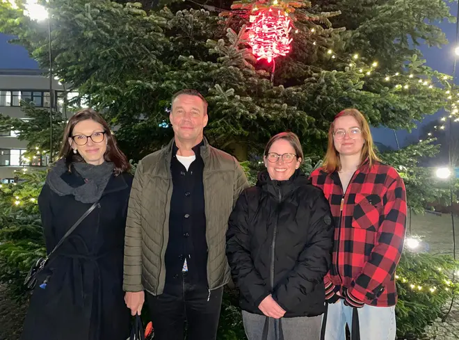 Tre kvinnor och en man står utomhus framför en julgran.