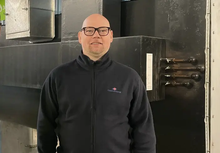 En man i svart tröja och glasögon som står i en industrimiljö. 