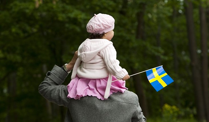 Liten flicka i klädd i rosa sitter på en mans axlar med en Sverigeflagga i handen. 