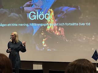 En person framför en projektorduk med texten "Glöd" och "”ågan att hitta mening, hålla engagemanget och fortsätta över tid”".