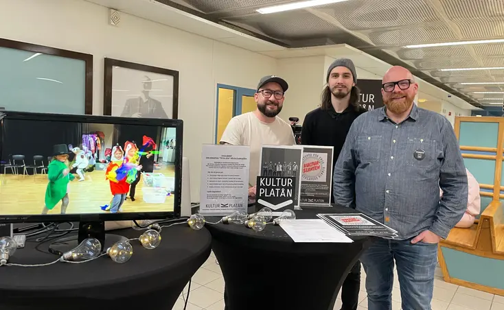 Tre män står bakom två svarta podier med en skärm och flera bordspratare.