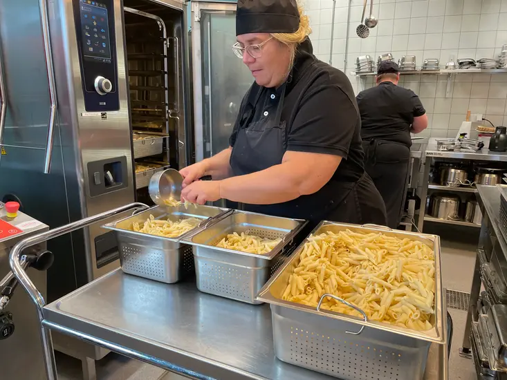 En kvinna som står i ett storkök och lagar mat. 