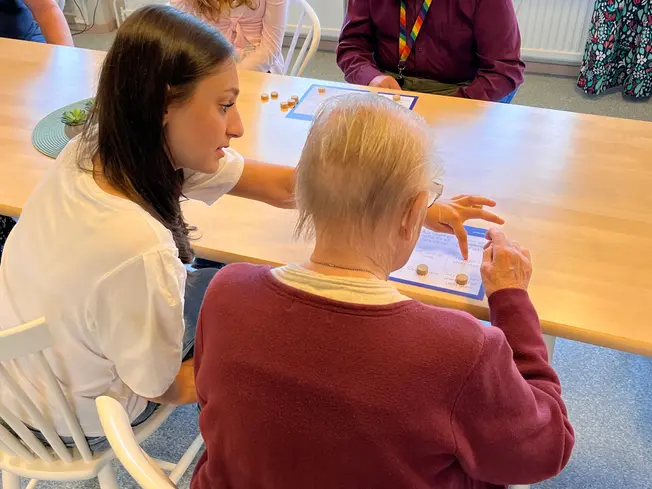 Foto på en elev som hjälper en äldre dam att spela bingo.