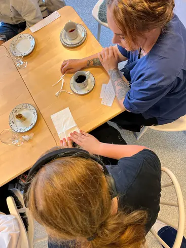 Foto från ovan på en anställd och en elev, de viker en servett och pratar.