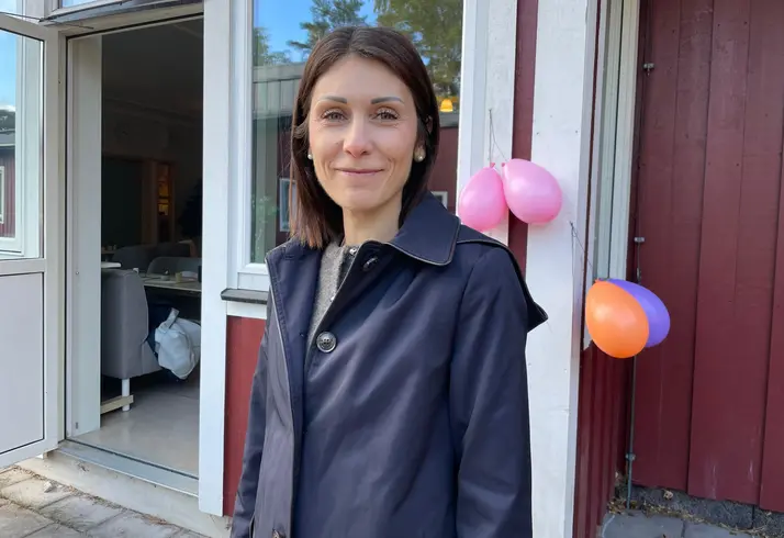 En kvinna som leende tittar in i kameran. I bakgrunden syns ballonger.