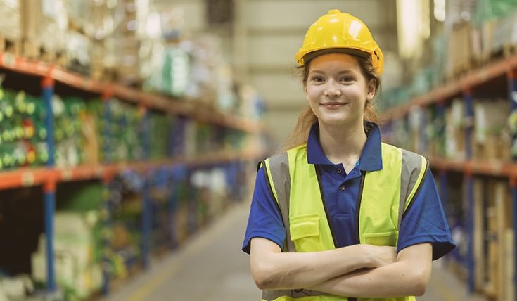 Ung kvinna står på ett lager i arbetskläder.