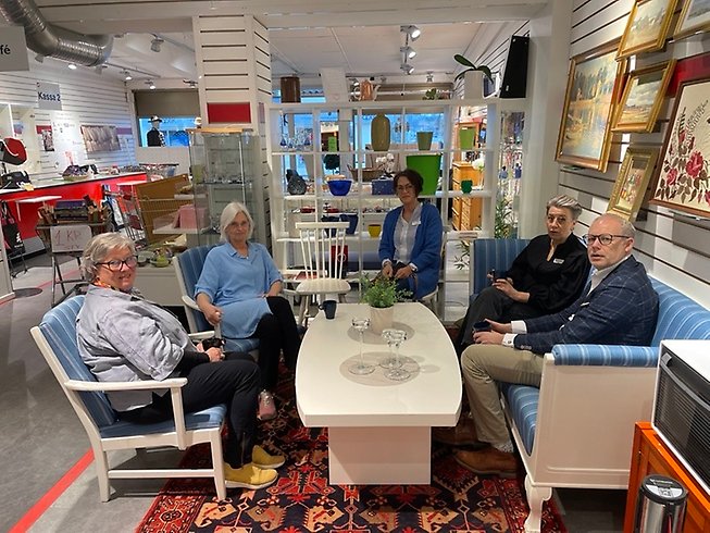 Fem personer sitter runt ett fikabord i butiken.