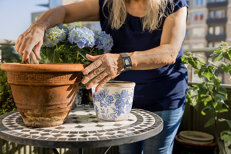 Person planterar blommor. På armen har hon en larmknapp. 