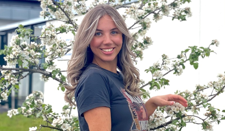 Ung kvinna framför en byggnad med körsbärsträ i bakgrunden