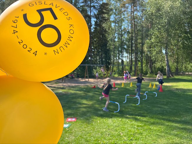 Ett foto på elever som tränar i gräset, vid sidan syns kommunens guldfärgade ballonger där det står 50 år.