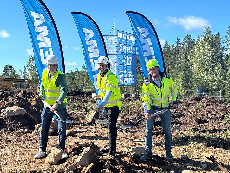 tre personer står framför Biltema-flaggor tar ett spadtag