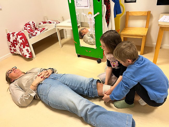 Foto på en vuxen som ligger på golvet och ett barn som undersöker.